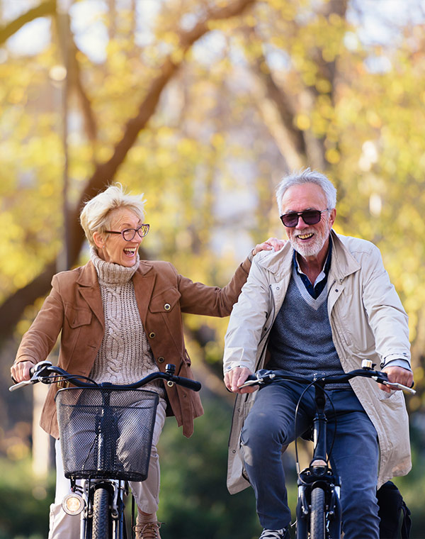 smiling senior couple riding bicycles in the park retire well